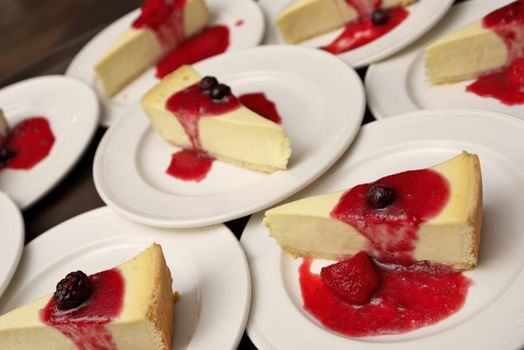 High Angle Full Frame Image of Plates of Sliced Cheesecake with Strawberry, Cherry, Blueberry, and Blackberry Compote on White Dessert Plates
