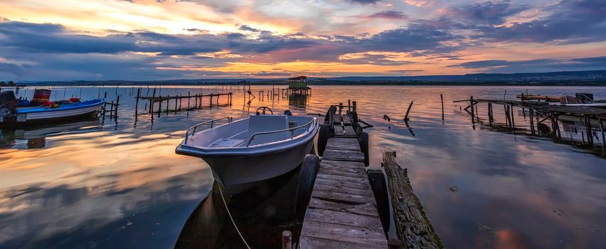 Amazing mood sunset at a lake coast with a boat at a wooden pier.