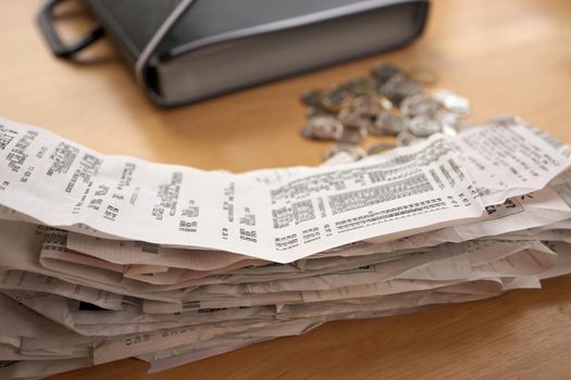 A stack of receipts in the Foreground with Coins and Accordion Folder Organizer in Background, symbolic of tax filing, business expenses, claims, and accounting. Low angle