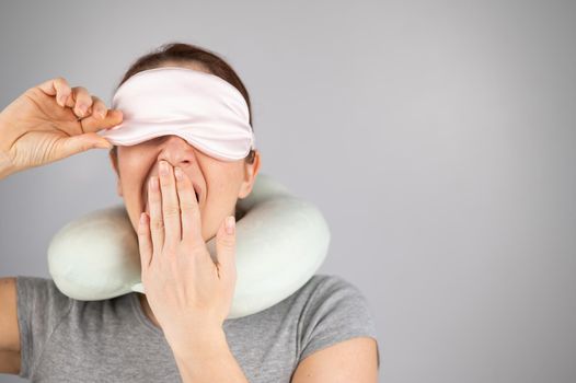 Caucasian woman yawns with travel pillow and sleep mask on white background