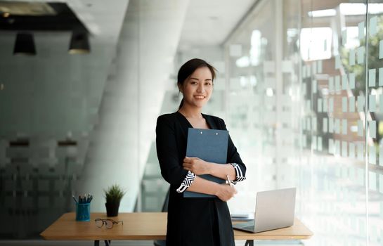 Portrait confidence business asian woman standing while working for financial accounting with laptop and calculator.
