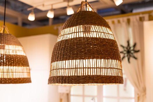 A stylish wicker wooden chandelier in boho and Bali style hangs on the ceiling near a white canopy made of weightless tulle.