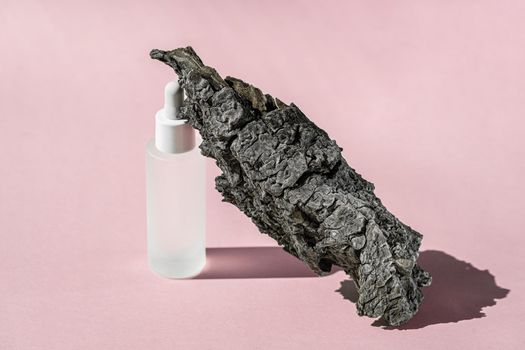 Serum cosmetic bottle mockup with bark tree on pink background, shadow from sun, natural light from windows. Transparent liquid product in glass bottle with dropper, product presentation