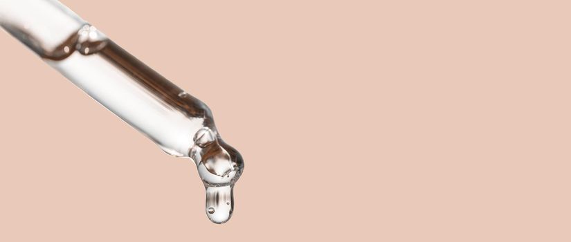 Cosmetics dropper, falling drop close up. Closeup of cosmetic pipette with essential oil dropping, serum with peptides on beige background. Beauty skin care product. Banner