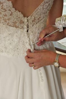 Close up of Mother of Bride's Hands Doing Final Buttoning of Bride's Wedding Dress. High quality photo