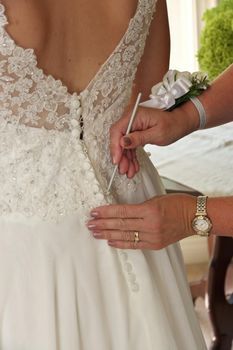 Close up of Mother of Bride's Hands Doing Final Buttoning of Bride's Wedding Dress. High quality photo