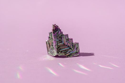 Synthetic bismuth Bismuthumcrystal with iridescent oxide film on pink background close up isolated. Amazing colorful shiny rainbow Bismuth Gemstone mineral. Banner