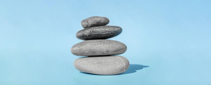 The balancing cairn - symbol of harmony, tranquility and relaxation, concept of meditation. Stack of spa hot stones. Balanced pebble stones for spa treatments on blue background.