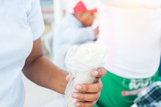 Closeup of the hands of a Nicaraguan woman holding a traditional dish called quesillo tucked in a plastic bag, a thin sheet of artisanal mozarella cheese on a corn tortilla