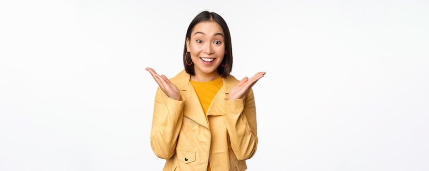 Image of asian woman looking surprised, amazed reaction, shocked face, standing over white background. Copy space