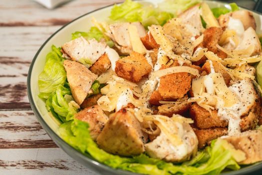Exquisite Caesar salad with small bites of chicken and a traditional aioli sauce in a small bowl on a rustic table. High view. Close-up detail. Gourmet concept.