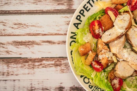 Exquisite variation of Caesar salad with thin slices of chicken, cherry tomatoes and a gourmet aioli sauce in a small bowl on a rustic table. Top view. Close-up detail.Vertical orientation.