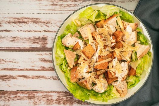 Exquisite Caesar salad with small bites of chicken and a traditional aioli sauce in a small bowl on a rustic table. Top view. Copy space.