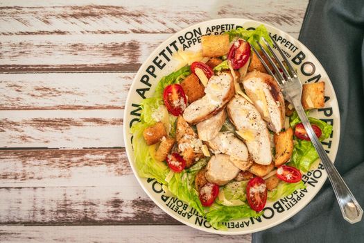 Exquisite variation of Caesar salad with thin slices of chicken, cherry tomatoes and a gourmet aioli sauce in a small bowl on a rustic table. Top view. Copy space