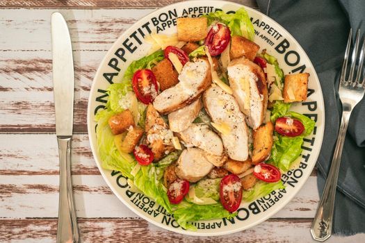 A variation of Caesar salad with thin slices of chicken, cherry tomatoes and a gourmet aioli sauce in a small bowl on a rustic table.