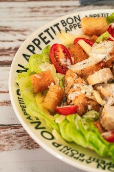 Exquisite variation of Caesar salad with thin slices of chicken, cherry tomatoes and a gourmet aioli sauce in a small bowl on a rustic table. High view. Vertical orientation. Close up