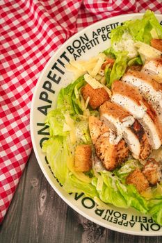 Caesar salad with thinly sliced chicken breast and traditional aioli on a plate that says bon apetite on a rustic table. High view. Close-up detail. Vertical orientation.