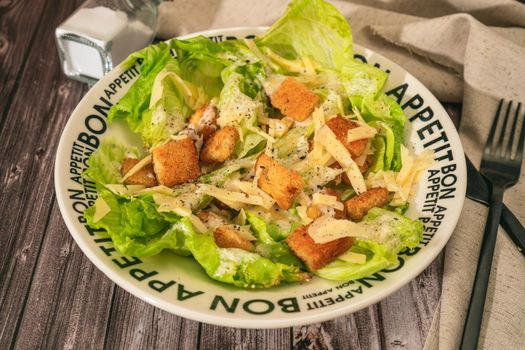 Exquisite traditional Caesar salad of lettuce, toasted bread and fine Parmesan cheese with a garlic aioli and olive oil in a bowl that says Bon Appetite in French. View at 45 degrees.