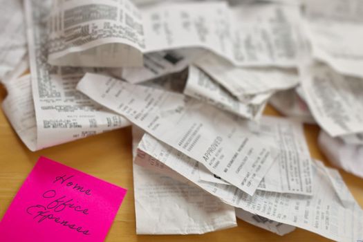 High Angle View of Pile of Receipts with Home Office Expenses Pink Sticky Note on Table in Foreground