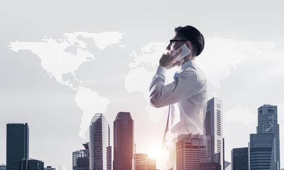 Double exposure of elegant businessman standing facing the city and talking his mobile phone