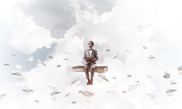 Funny man in red glasses and suit sitting on book and paper planes flying around