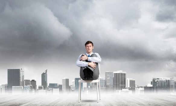 scared businessman sitting on a chair with his hands clasped his knees