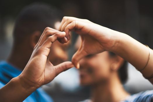 Cropped shot of a young couple making a heart gesture with their hands outdoors.