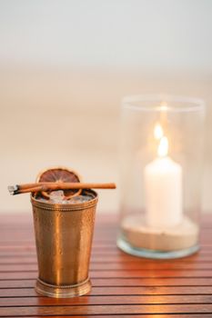 Hand with cocktail, Alcoholic drink with ice, orange and cinnamon on the beach.