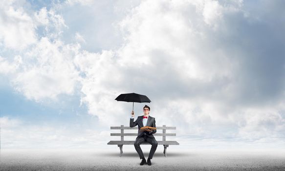 young student with umbrella and book sits on a bench