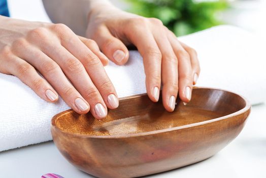 Closeup female hands in wooden bowl with water. Spa procedure and relaxation. Female hands preparing for manicure. Professional nail care and beautician service. Beauty and hygiene concept