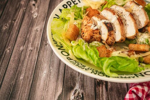 Caesar salad with thinly sliced chicken breast and traditional aioli on a plate that says bon apetite on a rustic table. High view.