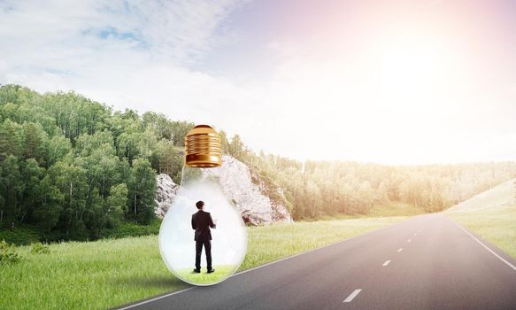 Young businessman trapped inside of light bulb on asphalt road