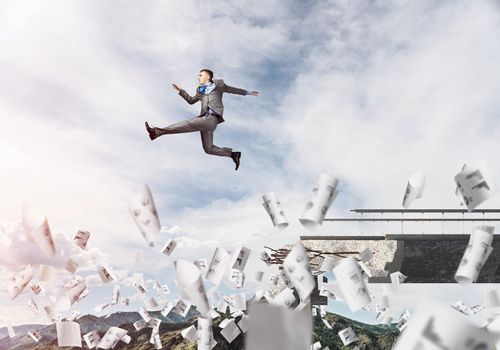 Businessman jumping over gap in bridge among flying papers as symbol of overcoming challenges. Skyscape with sunlight and nature view on background. 3D rendering.