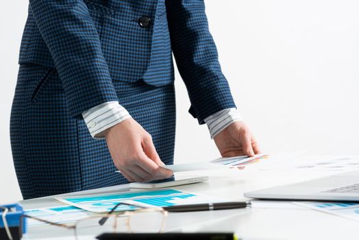 Businesswoman standing near office desk with laptop and documents. Financial audit and consulting. Corporate manager in suit working with online business analytics. Investment and stock trading