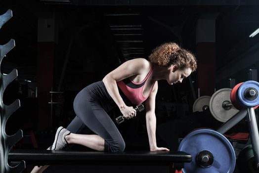 Woman bodybuilder engaged with dumbbells in the gym.