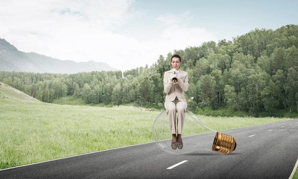 Attractive woman playing trumpet brass on asphalt road. Young businesslady in white business suit and gloves sitting on big light bulb with music instrument. Musician practicing and performing outdoor