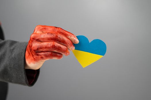 Woman with hands covered in blood holding a heart with the flag of ukraine on a white background