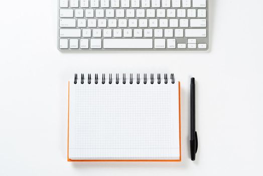 Top view of businessman workplace. Spiral notepad, pen and computer keyboard on white surface. Education, creativity and working concept with copy space. Finance and investment background.