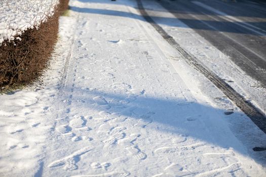 Sidewalk covered with a thick layer of fresh snow. Highway covered with frozen snow and ice. Dangerously slippery due to lack of snow removal.