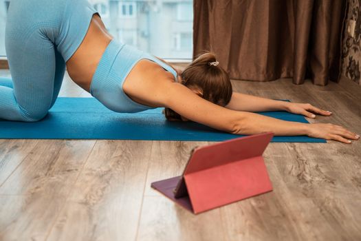 Young athletic attractive woman practicing yoga doing exercises. Works out at home or in a yoga studio, sportswear, blue pants and a full-length top indoors. Healthy lifestyle concept.