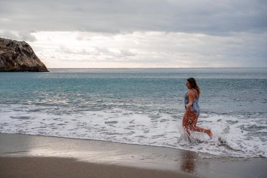 A plump woman in a bathing suit enters the water during the surf. Alone on the beach, Gray sky in the clouds, swimming in winter