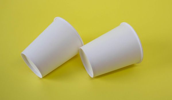 Two small white paper cups on a yellow background.