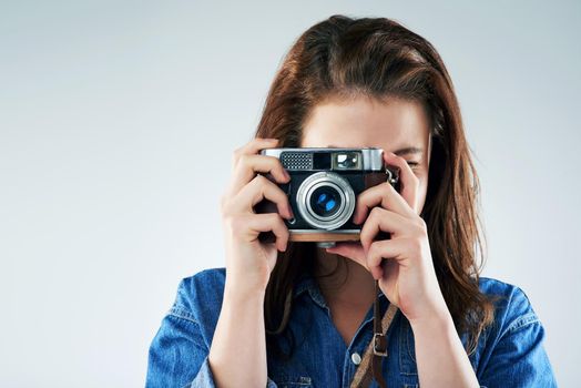 Studio portrait of a young woman using a vintage camera against a grey background.