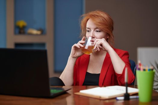 Businesswoman drinking tea while working on laptop at the office