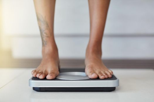 Closeup shot of a woman weighing herself on a scale at home.