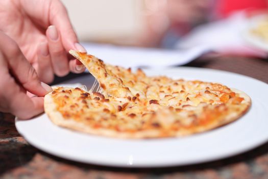 Female hand tearing off appetizing hot slice of pizza with cheese closeup. Street food concept
