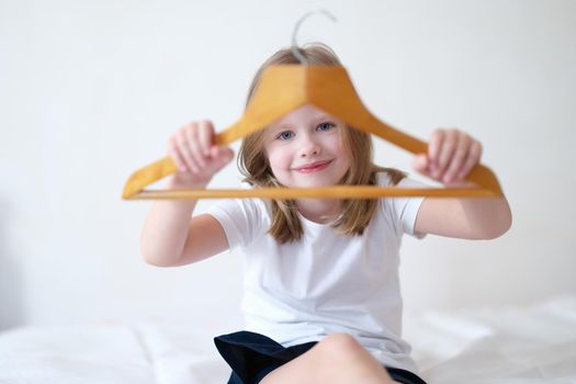Little girl holding wooden clothes hanger in hands. Children online shopping concept