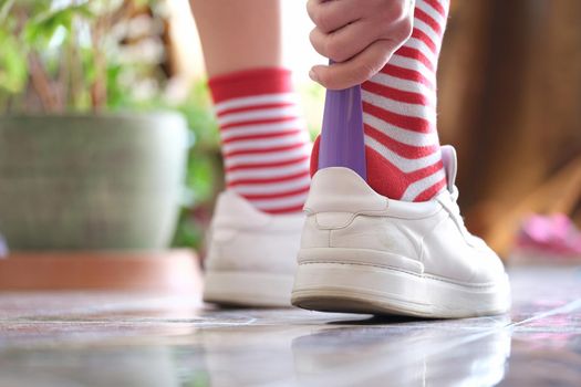 Man in striped socks putting on white sneakers with shoehorn closeup. Shoe accessories concept