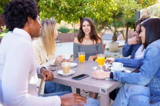 Multi-ethnic group of friends having a drink together in an outdoor bar. One of the men shows something on his smartphone to his friends.