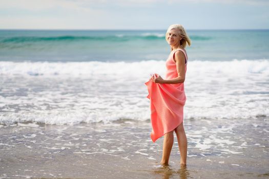 Older woman enjoying her free time looking at the sea from the shore of the beach.. Elderly female enjoying her retirement at a seaside retreat.